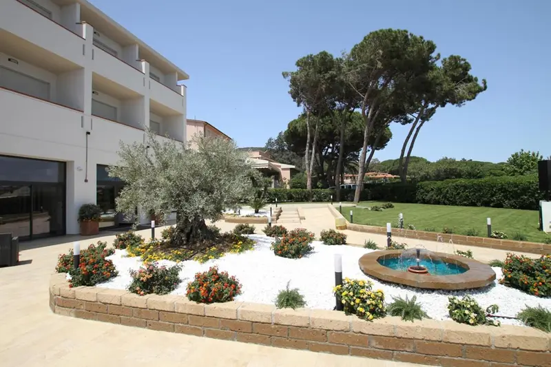 Un bâtiment blanc avec des arbres et des arbustes dans un jardin soigné.