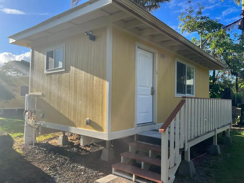 Une petite maison jaune sur pilotis avec une terrasse en bois et des marches d'accès.