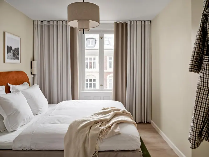 Une chambre lumineuse avec un grand lit recouvert d'une couverture et de coussins blancs.