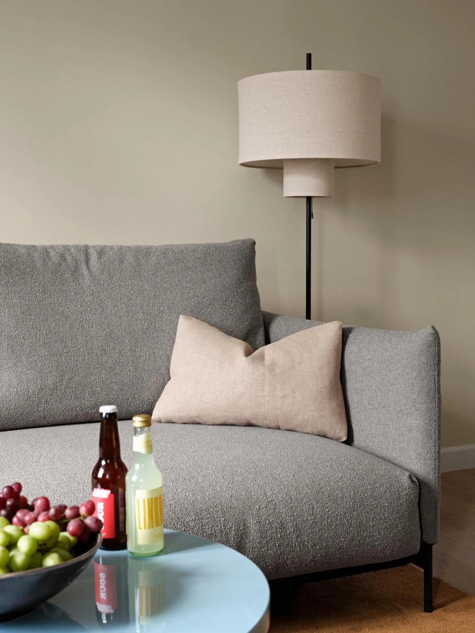 Un canapé gris avec des coussins et une table basse sur laquelle reposent des boissons et des fruits.