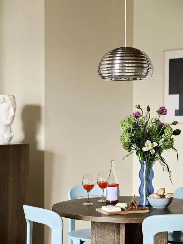 Une table ronde avec des verres de vin, une bouteille et des collations est mise en valeur par un luminaire suspendu.
