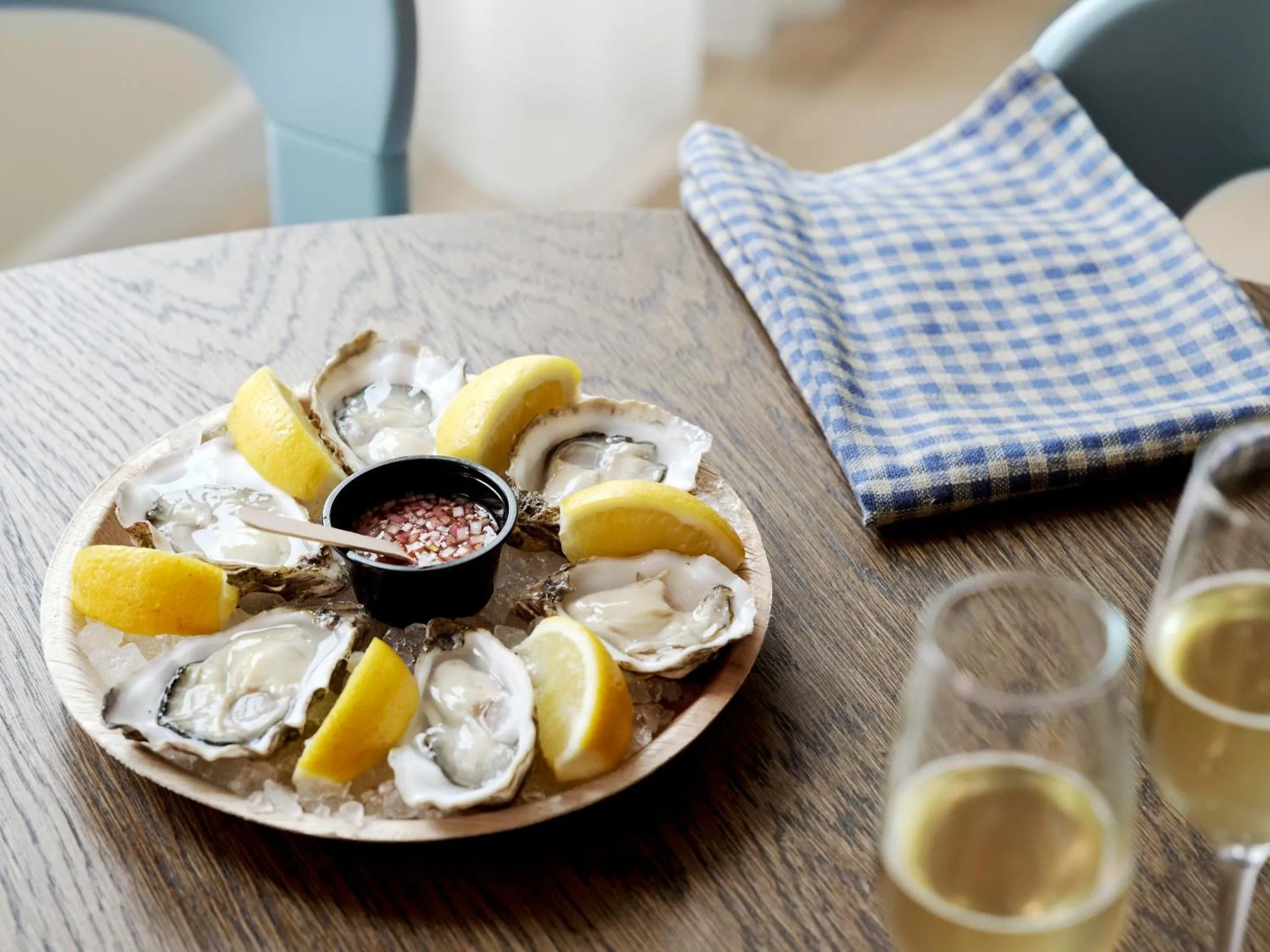 Une assiette d'huîtres fraîches est présentée sur une table en bois avec des citrons et un verre de vin.