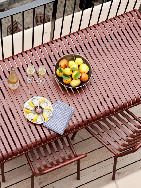 Une table en métal rouge avec des fruits et des amuse-gueules est mise en scène sur une terrasse.