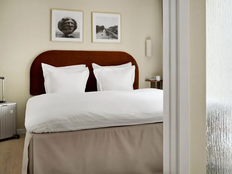 Un lit double avec une tête de lit en velours brun dans une chambre lumineuse.