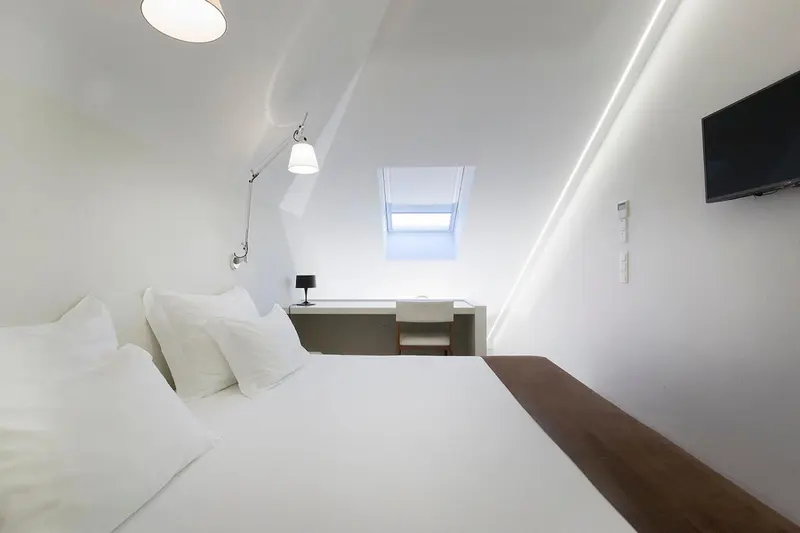Une chambre mansardée lumineuse avec un lit blanc et un bureau.