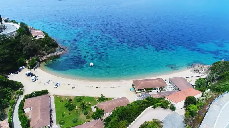 Vue aérienne d'une plage de sable fin bordée d'une eau turquoise et de bâtiments bas.