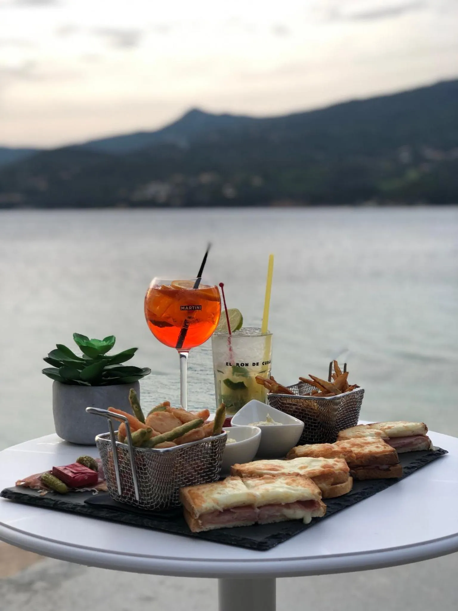 Une table ronde présente des boissons et des en-cas en bord de mer.
