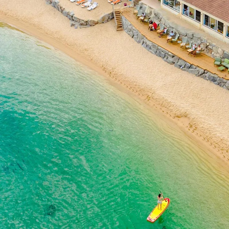 Vue aérienne d'une plage de sable fin bordée d'une eau turquoise et d'une terrasse en bois.