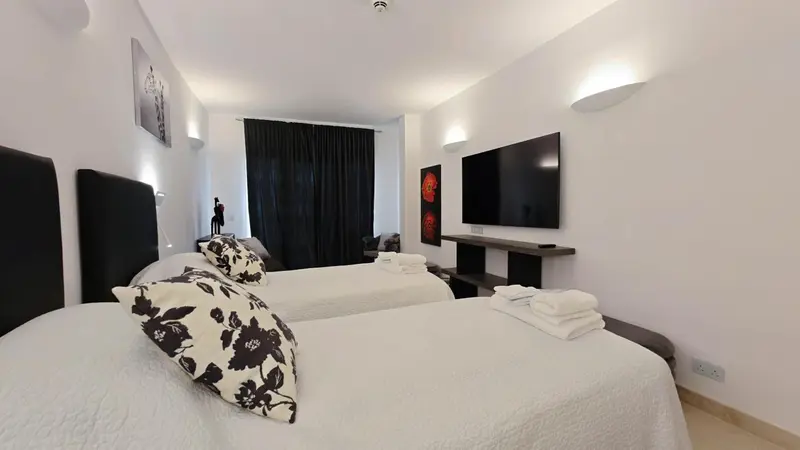 Une chambre lumineuse avec deux lits simples et une télévision murale.