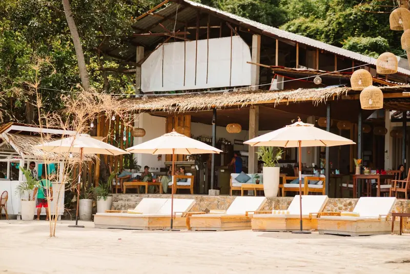 Terrasse de plage avec transats et parasols devant un bâtiment ouvert.
