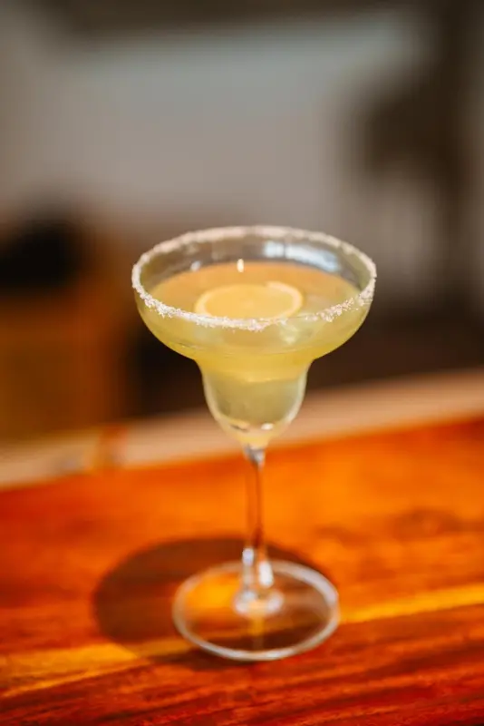 Un cocktail jaune servi dans un verre à margarita avec un bord sucré.