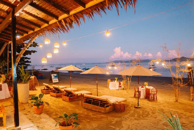 Terrasse de plage avec tables et chaises longues éclairées par des guirlandes lumineuses.