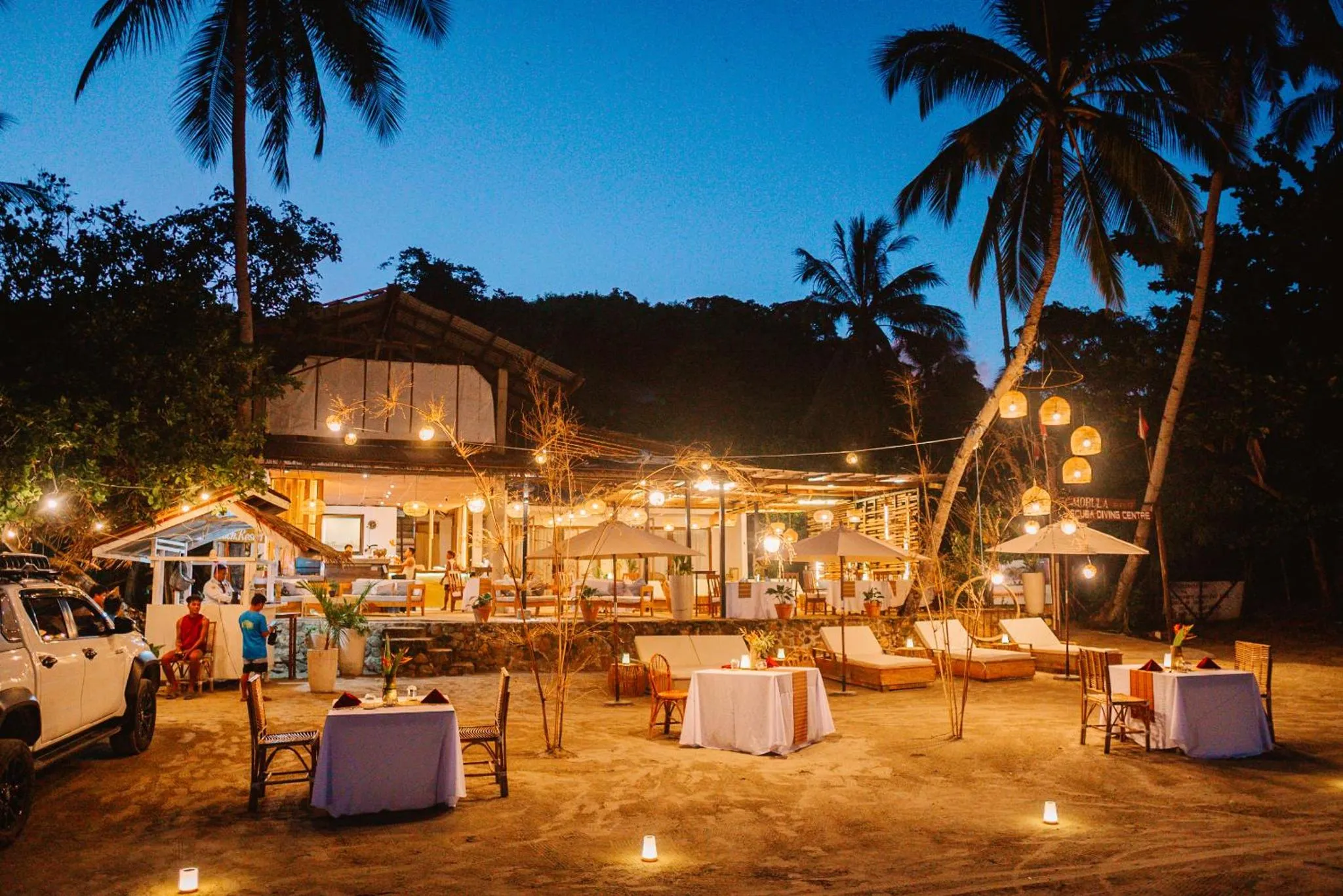 Terrasse lumineuse avec tables et chaises face à la mer au coucher du soleil.