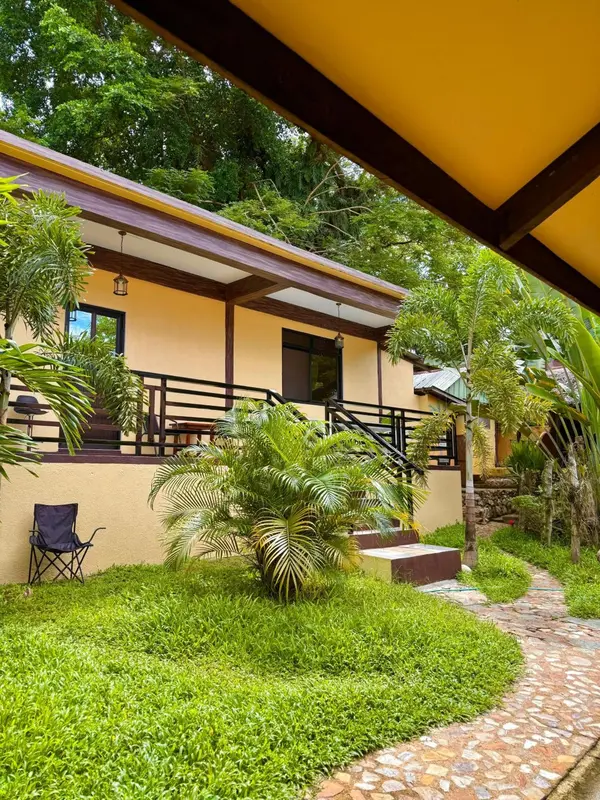 Une habitation jaune avec une terrasse et un jardin verdoyant.