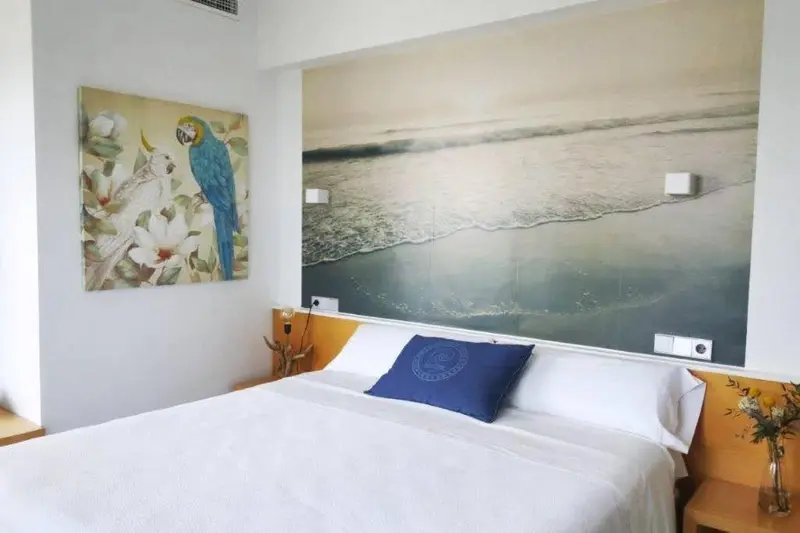 Une chambre lumineuse avec un grand lit et une décoration murale représentant un paysage marin et des oiseaux.
