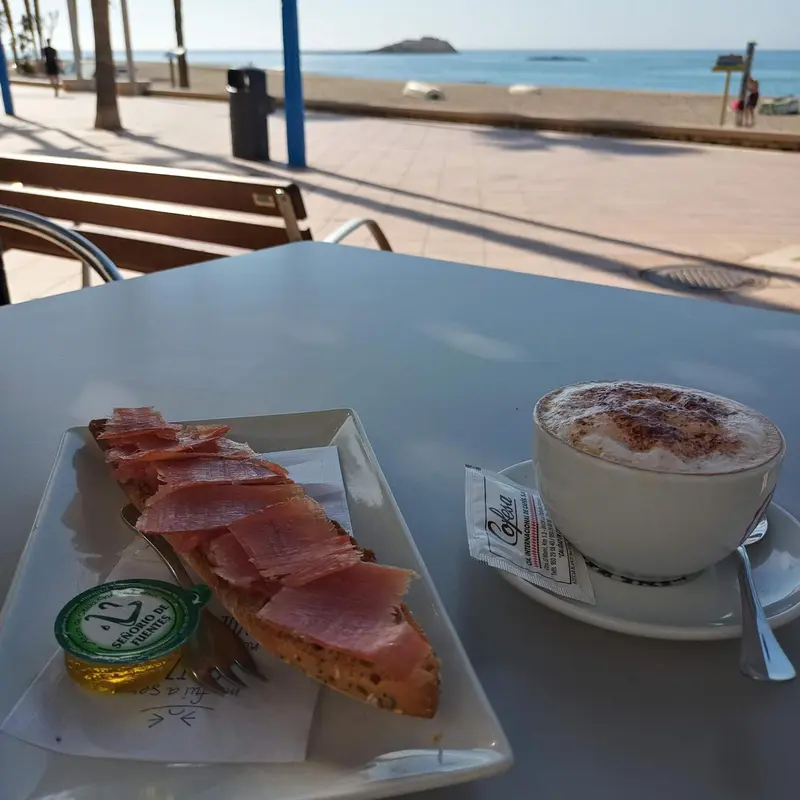 Une table en extérieur présente un petit-déjeuner avec une boisson au lait et des tranches de jambon.