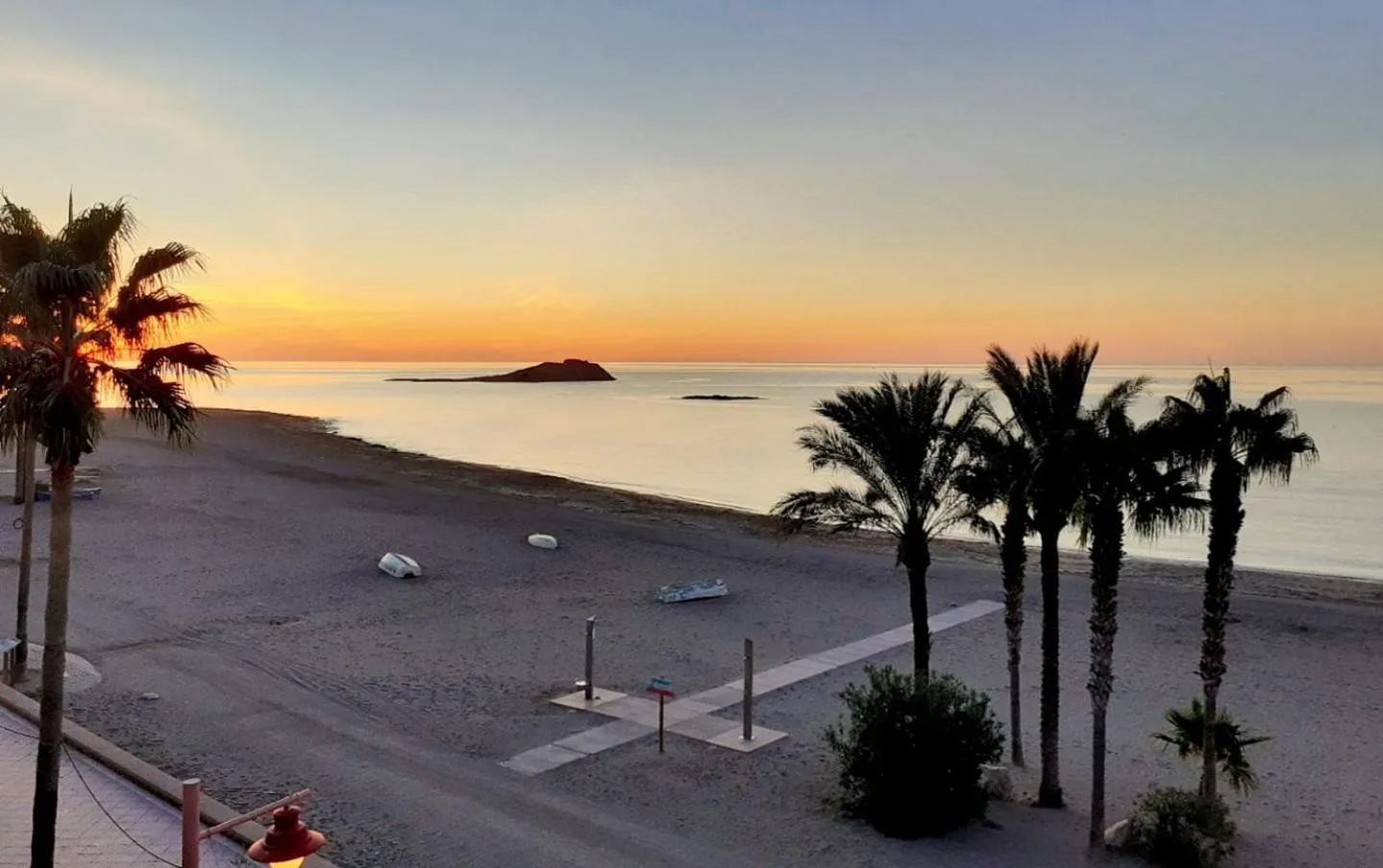 Coucher de soleil sur une plage de sable avec des palmiers et une vue sur la mer.