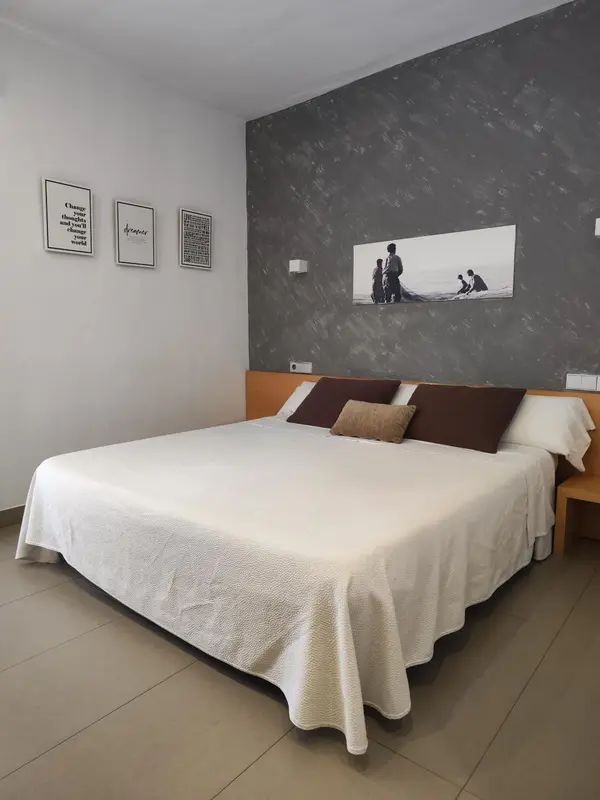 Une chambre lumineuse avec un grand lit recouvert d'une courtepointe blanche et de coussins.