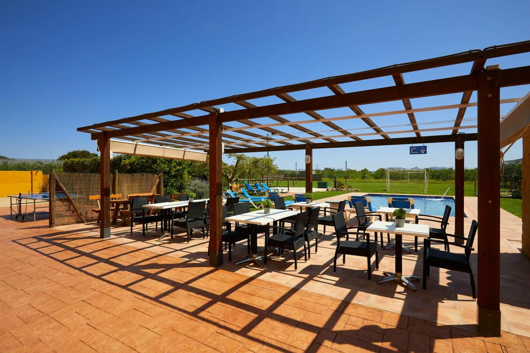 Terrasse ombragée avec tables et chaises près d'une piscine.