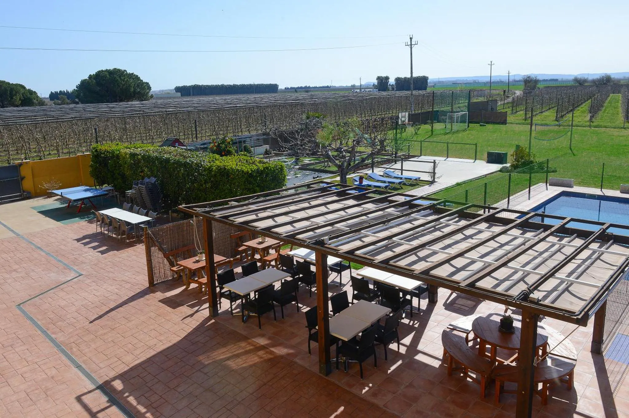 Terrasse ombragée avec tables et chaises, surplombant une piscine et un jardin.