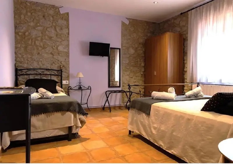 Une chambre avec deux lits simples et un mur en pierre.