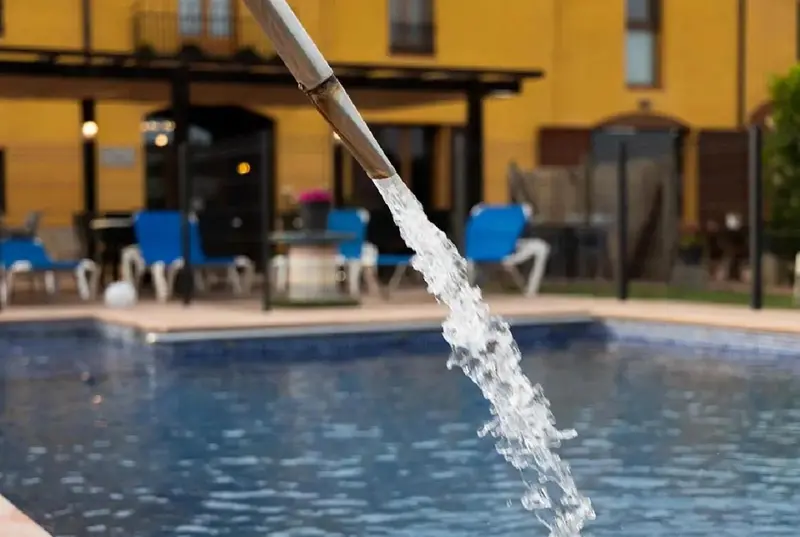L'eau jaillit d'une conduite au-dessus d'une piscine ensoleillée.