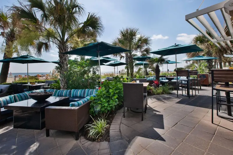 Espace extérieur aménagé avec des canapés, des tables basses et des parasols près de la mer.