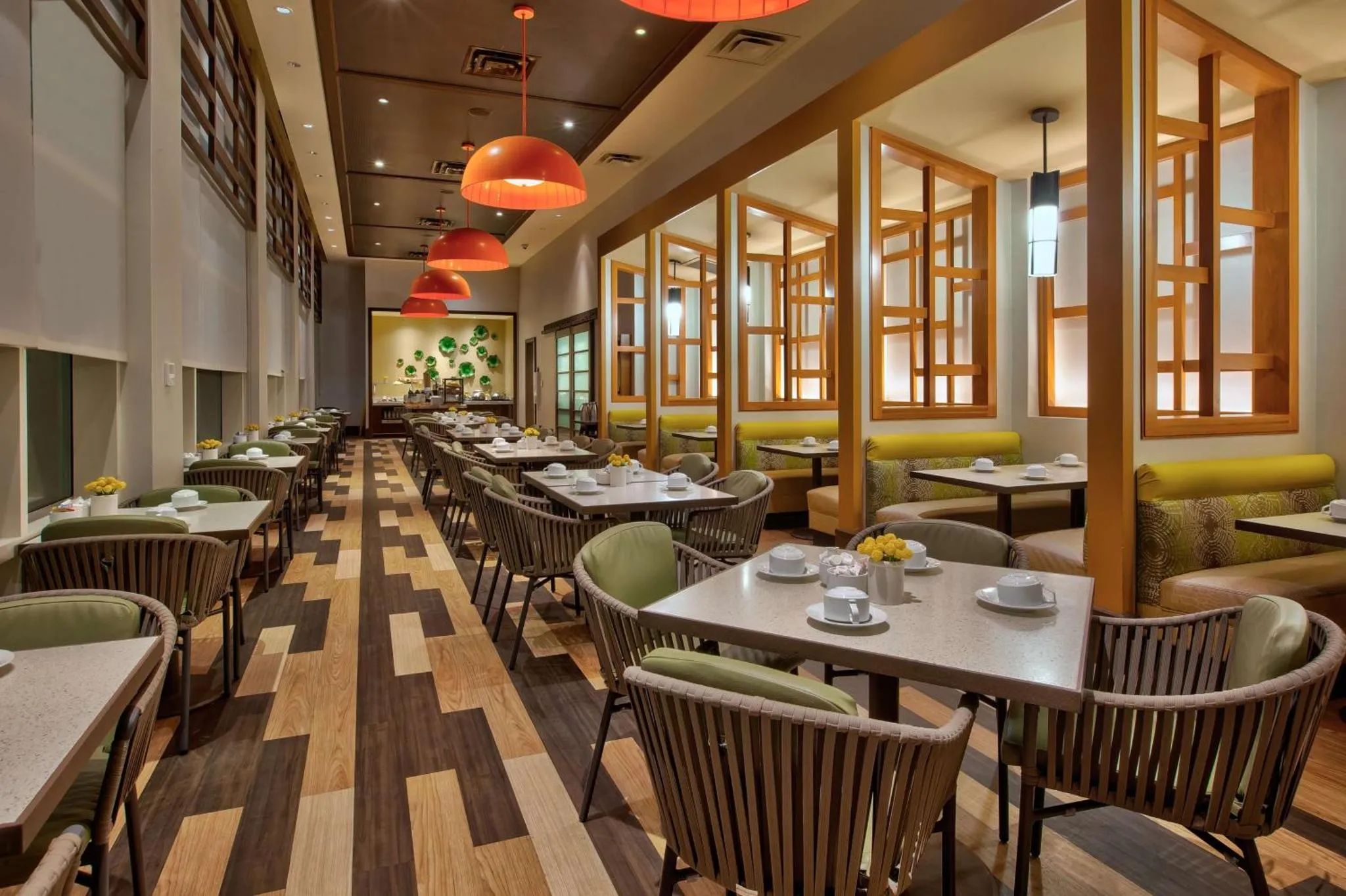 Une salle de restaurant lumineuse avec des tables dressées et des chaises vertes et grises.