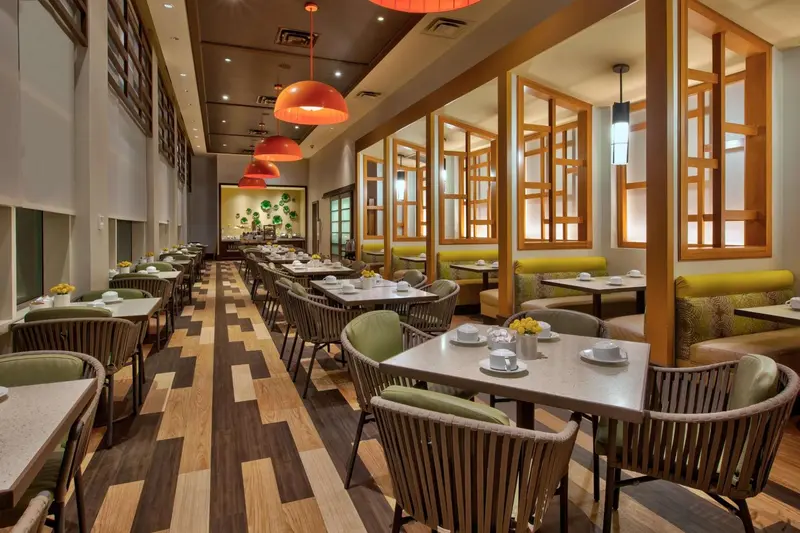 Une salle de restaurant lumineuse avec des tables dressées et des chaises vertes et grises.