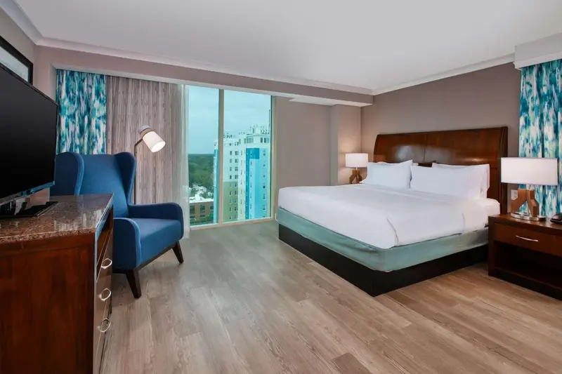 Une chambre d'hôtel lumineuse avec un grand lit et un fauteuil bleu.