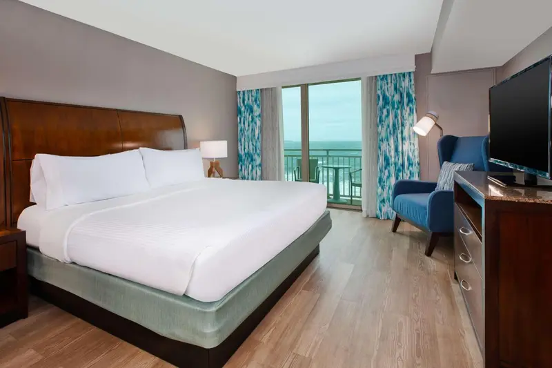 Une chambre lumineuse avec un grand lit et un fauteuil près d'une fenêtre.