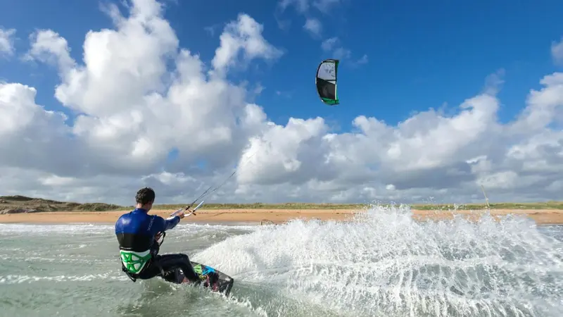 Une personne pratique le kitesurf sur une plage ensoleillée.