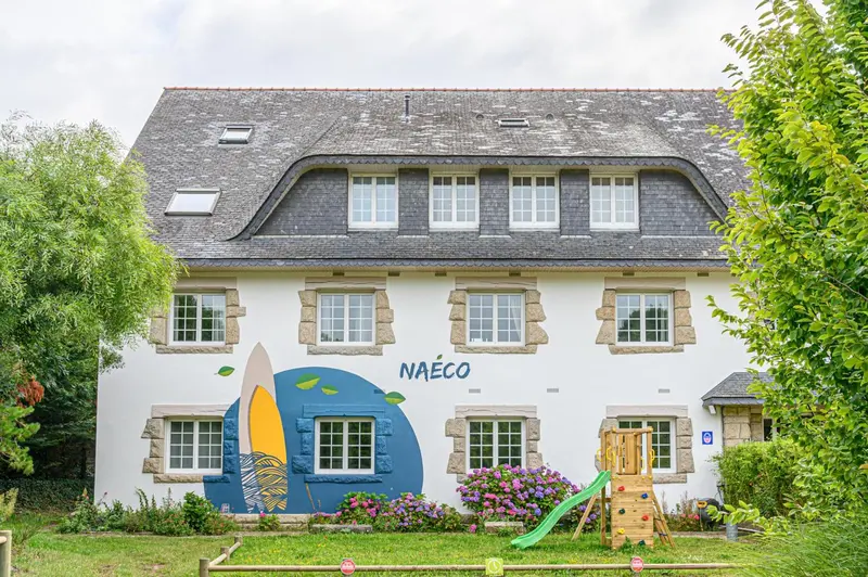 Façade d'un bâtiment blanc avec des fenêtres rectangulaires et une fresque colorée représentant des vagues et une planche de surf.