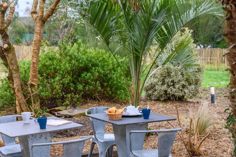 Une table avec des tasses, une théière et des viennoiseries est installée dans un jardin.