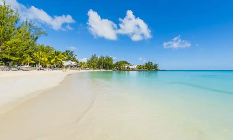 Plage de sable blanc bordée d'une eau turquoise sous un ciel bleu nuageux.