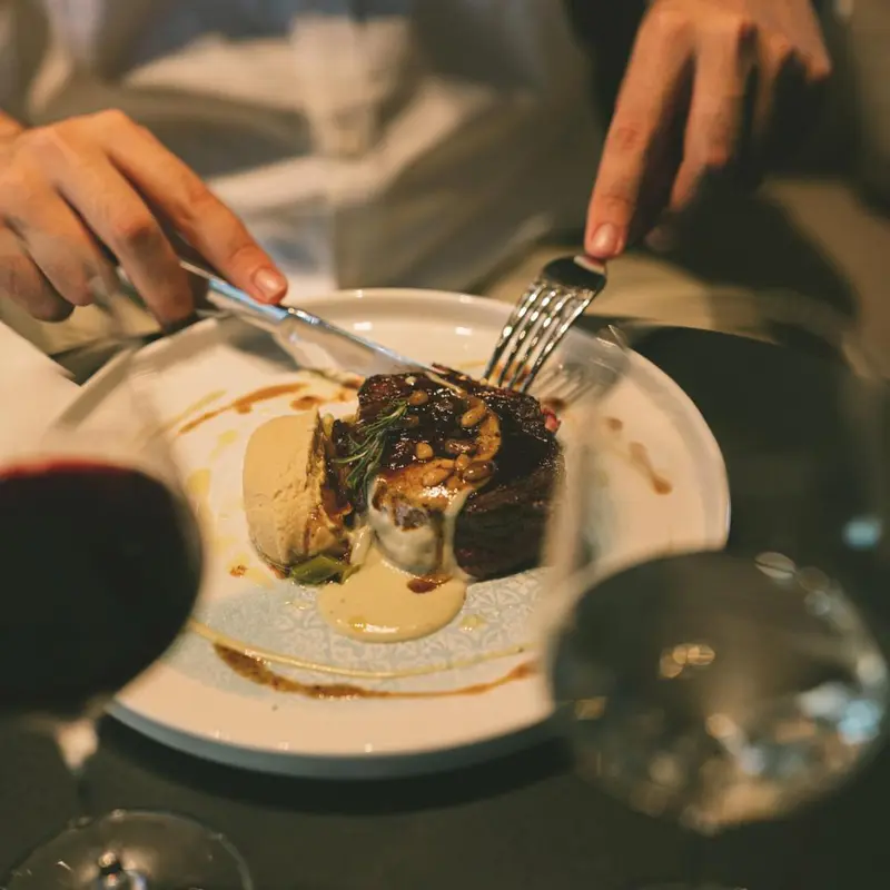 Une assiette de viande accompagnée d'une sauce et de légumes est présentée sur une table.