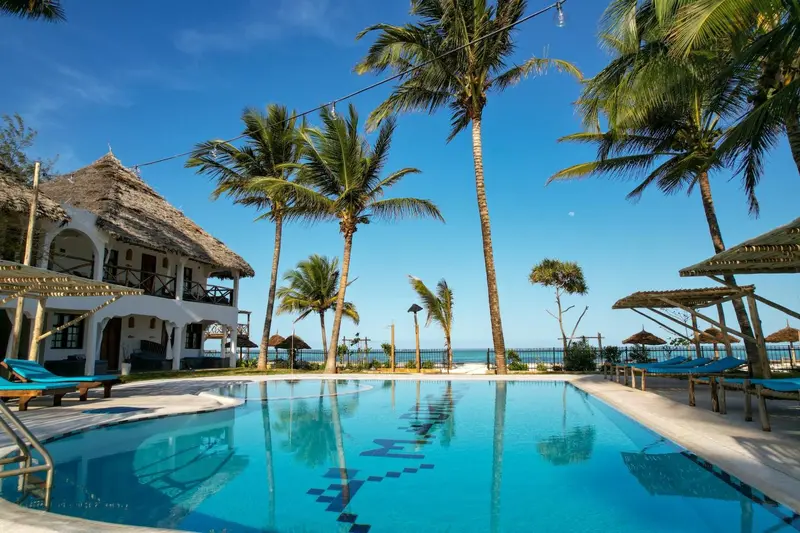 Une piscine turquoise reflète le ciel bleu et les palmiers environnants.