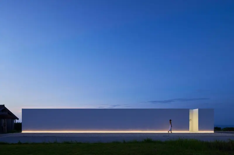 Bâtiment moderne éclairé la nuit avec une personne marchant vers l'entrée.
