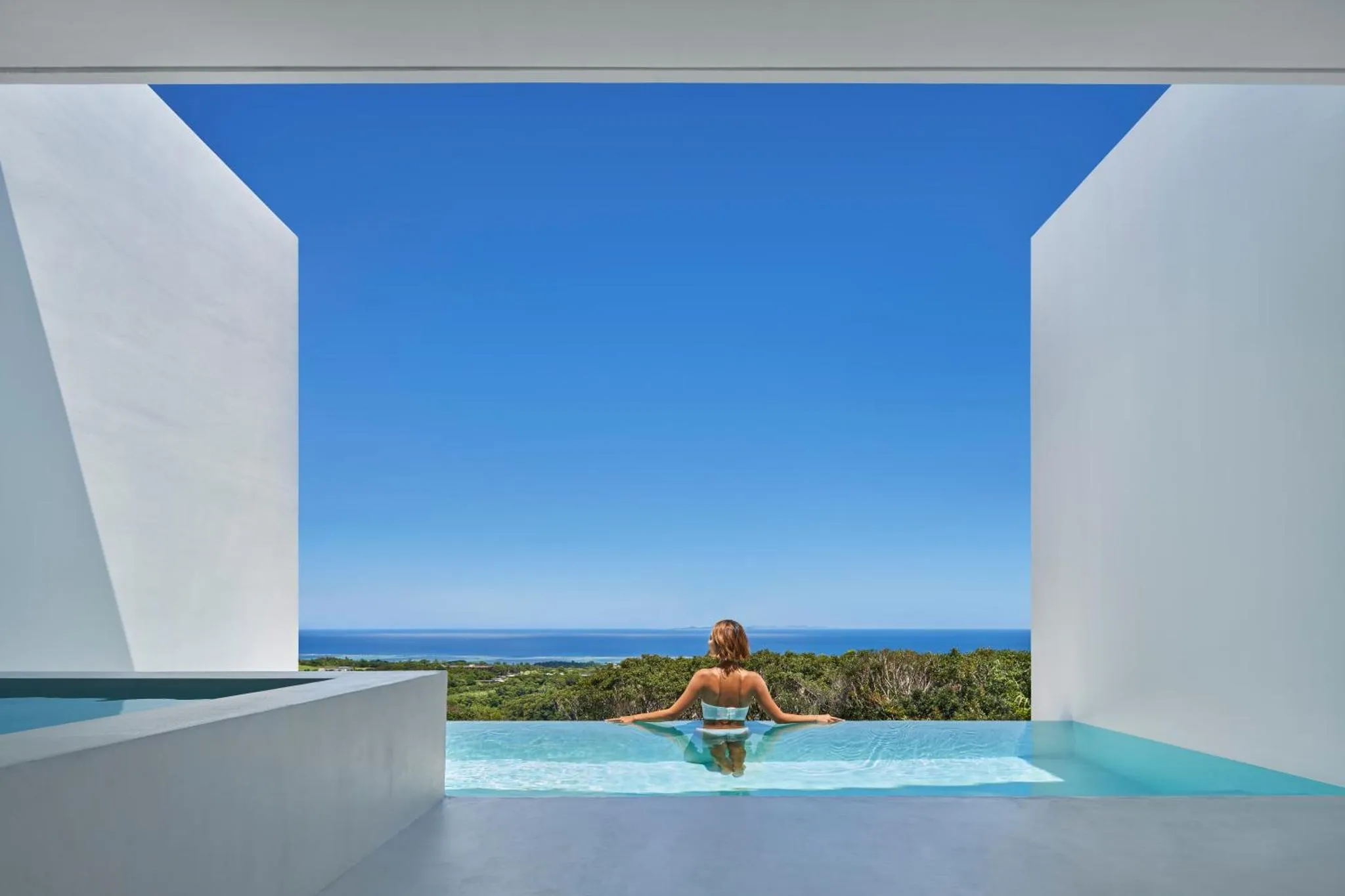 Une personne se détend dans une piscine à débordement avec vue sur la mer.