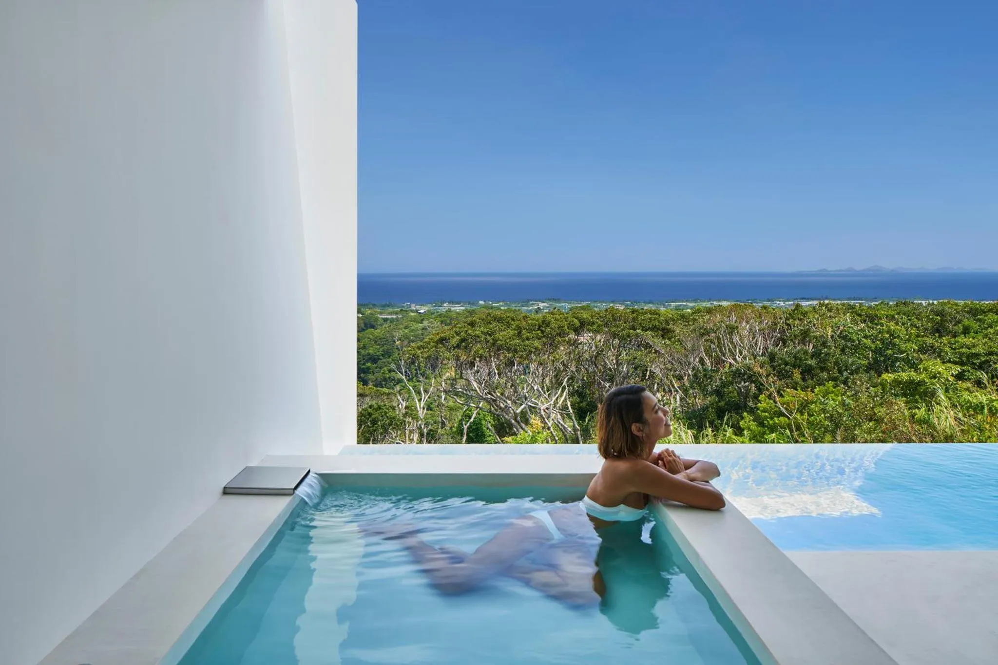 Une femme se détend dans un jacuzzi avec vue sur la mer et la végétation.