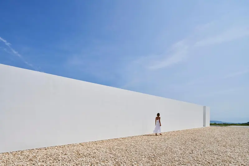 Une personne se tient devant un mur blanc et une plage de galets.