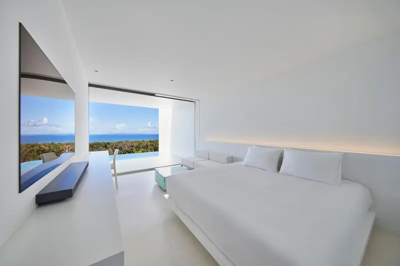 Chambre lumineuse avec un grand lit blanc et vue sur la mer.