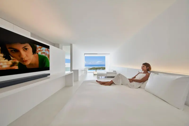 Une femme se détend sur un lit dans une chambre lumineuse avec vue sur la mer.
