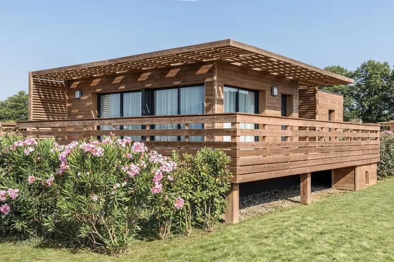 Maison en bois avec terrasse et végétation fleurie.