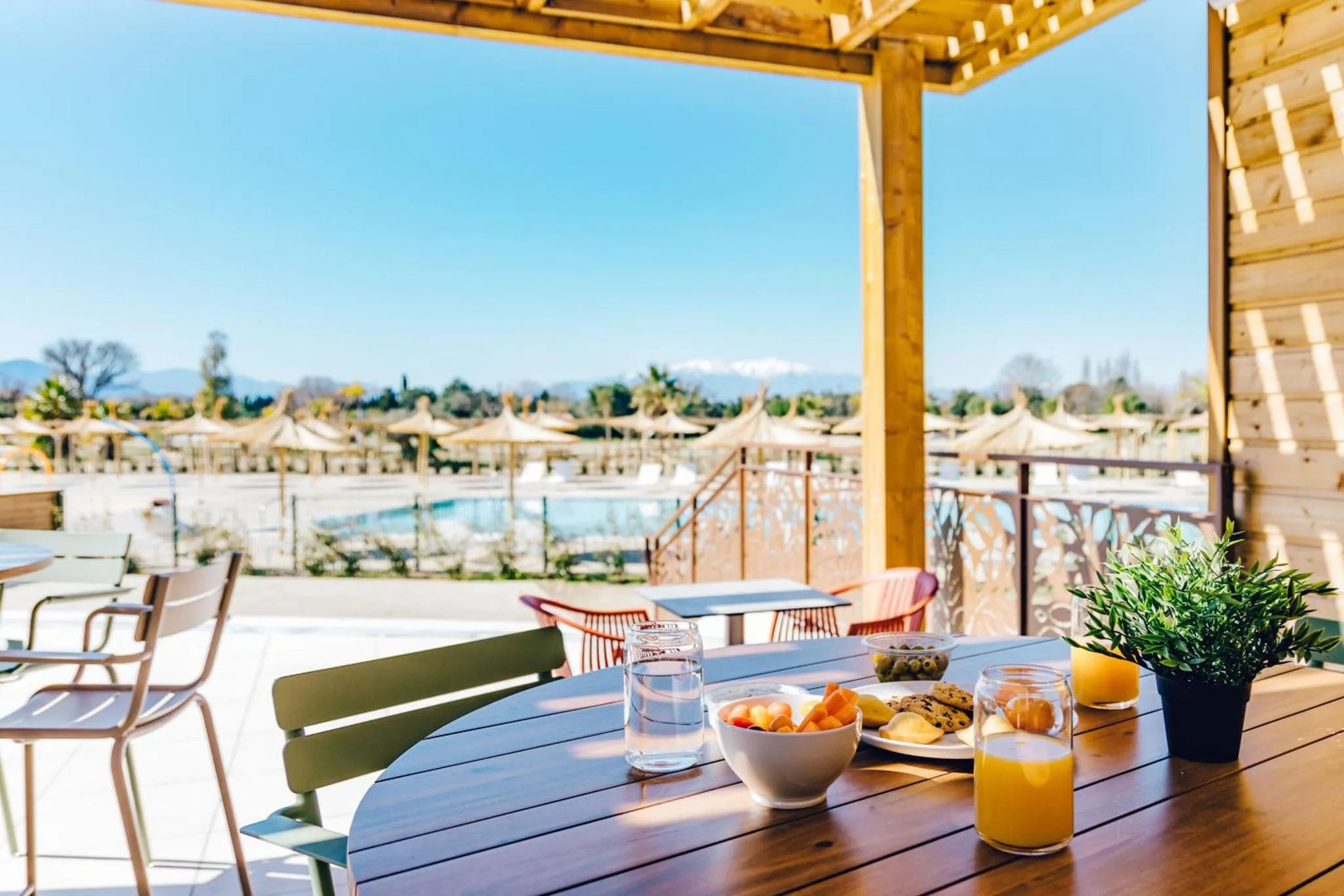 Une table en bois est dressée avec un petit-déjeuner face à une piscine et à la mer.