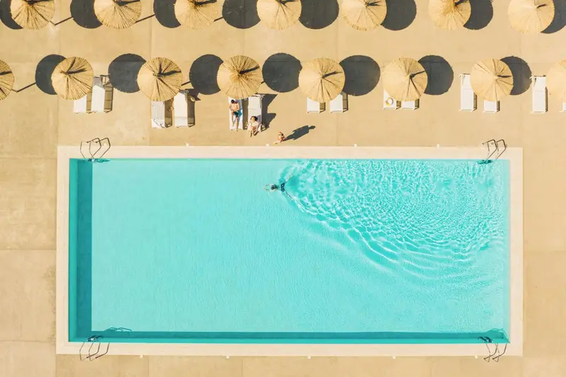 Vue aérienne d'une piscine rectangulaire entourée de transats sous des parasols.