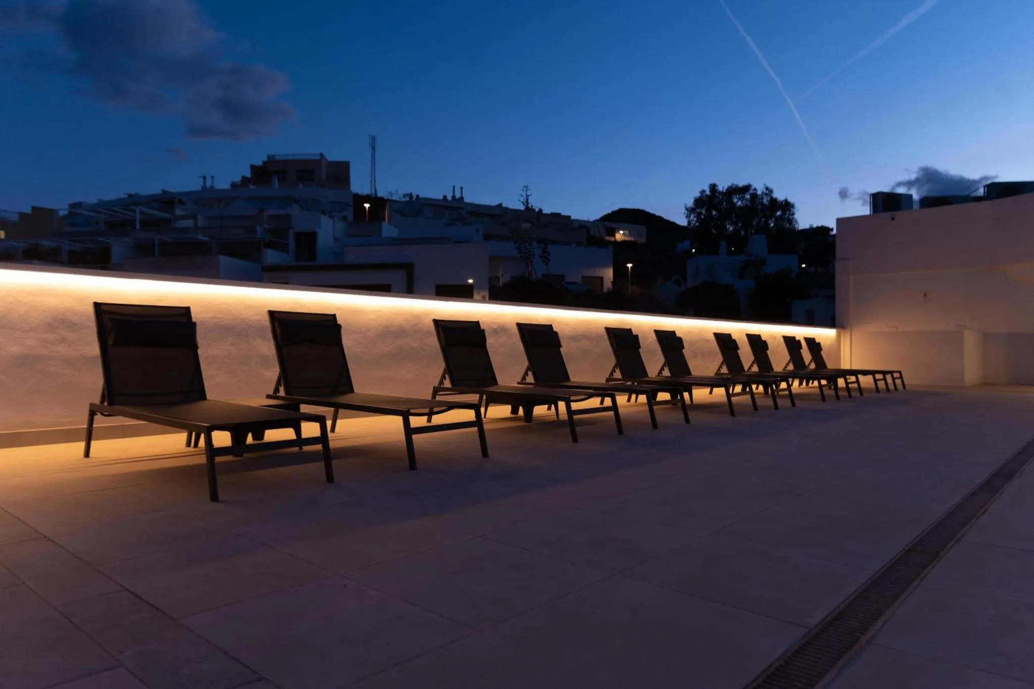 Transats alignés sur une terrasse éclairée au crépuscule, avec une vue sur un village.