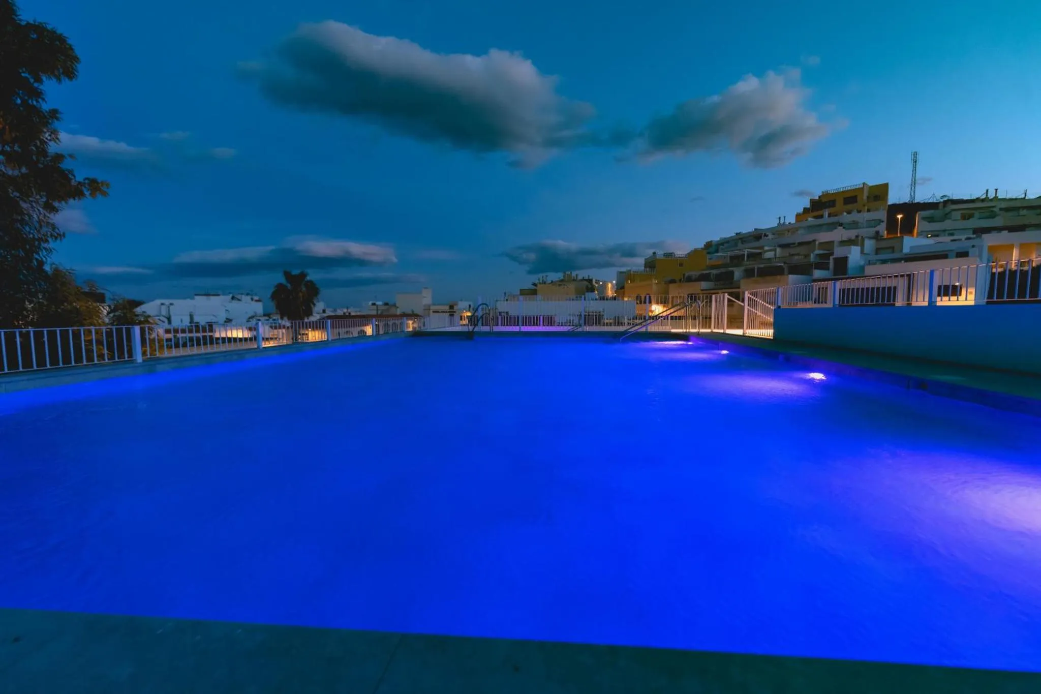 Piscine illuminée au crépuscule avec un bâtiment en arrière-plan.