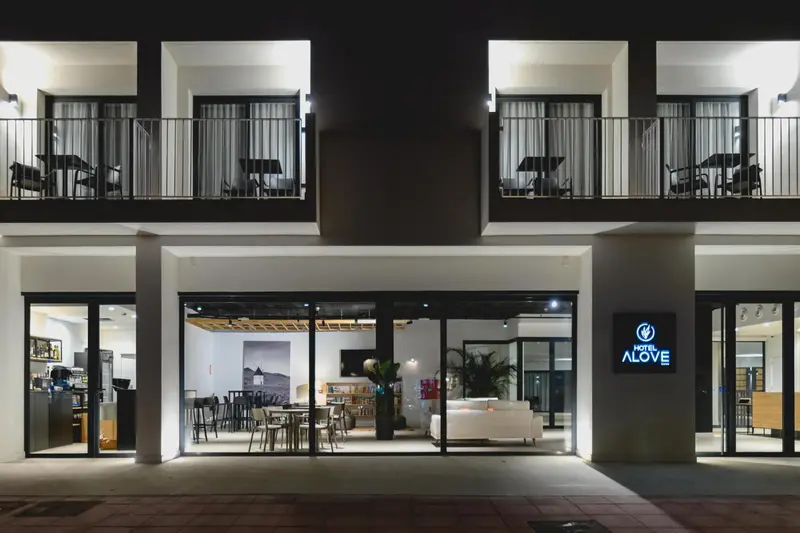 Façade d'un bâtiment blanc avec des balcons et une entrée lumineuse.