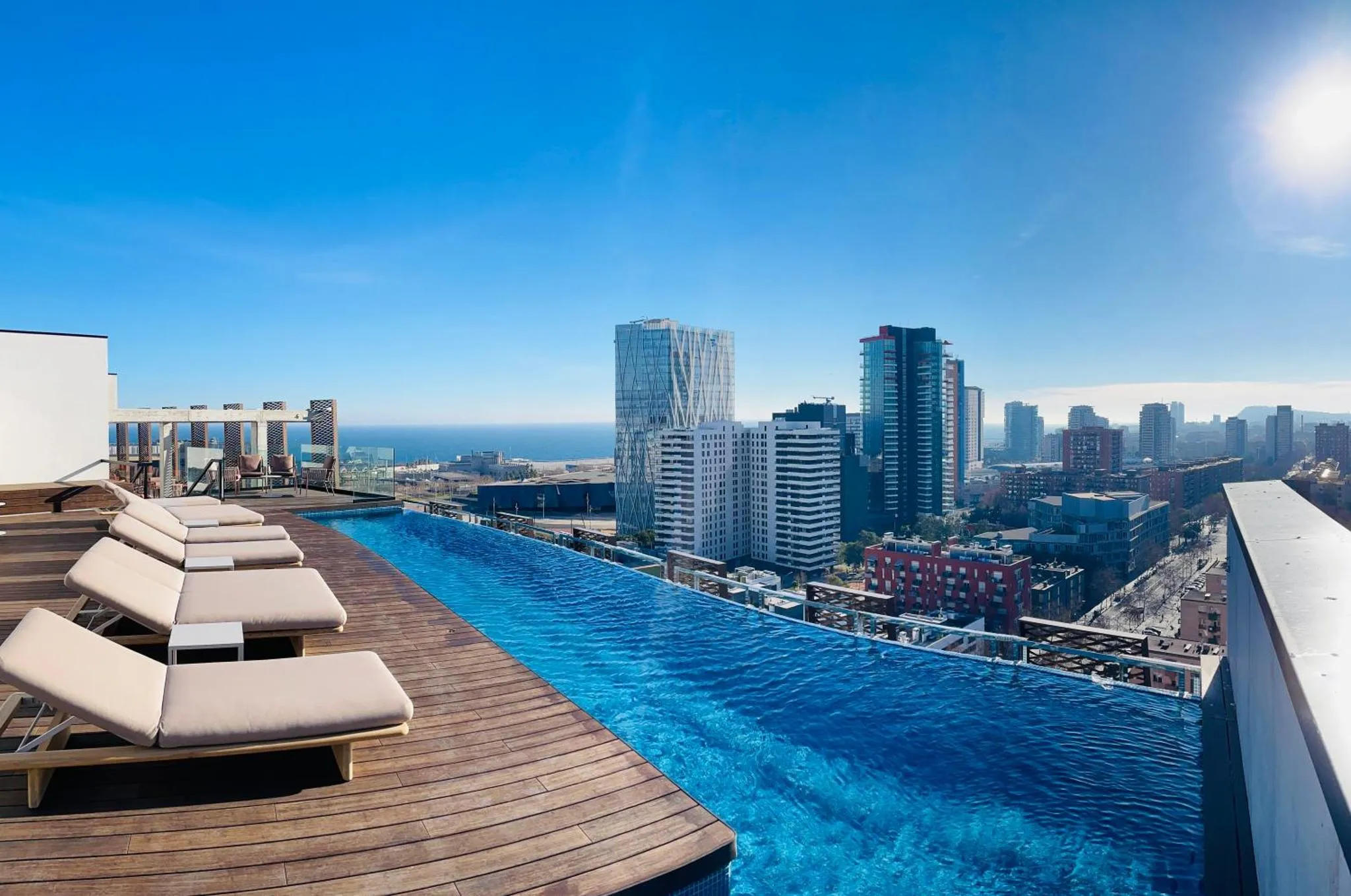Terrasse avec transats et piscine à débordement offrant une vue sur la ville et la mer.